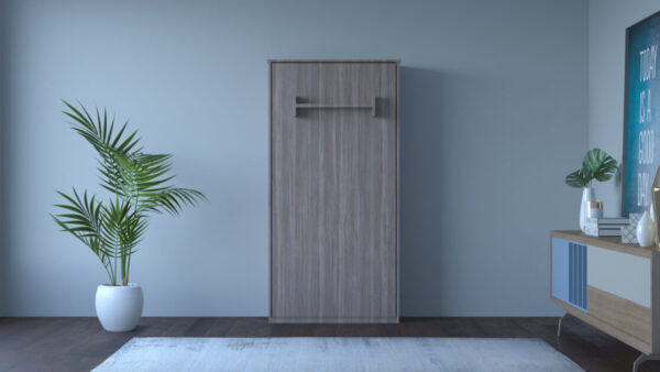 A vertical, wooden foldable bed closed and mounted against a plain wall, resembling a tall cabinet with a handle at the top.